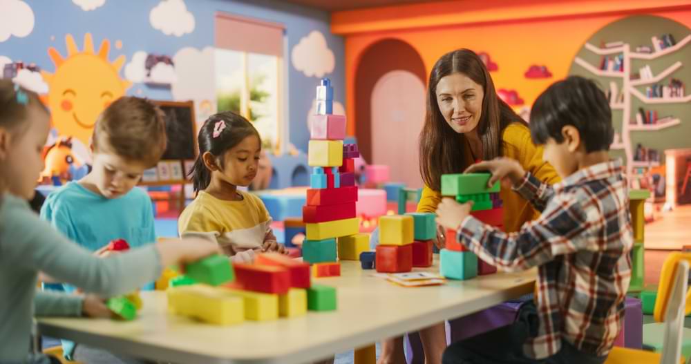 Children build with blocks while their teacher guides them in a bright classroom