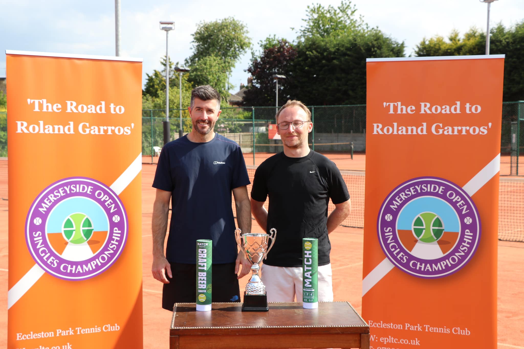 Finalists displaying trophies at the Merseyside Open under 'The Road to Roland Garros' tournament banners