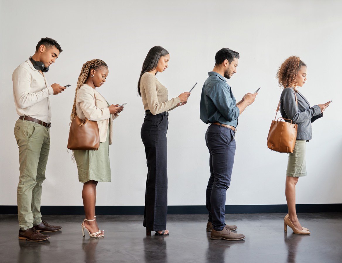 People waiting in line for a good or service. They are all looking at their mobile phones